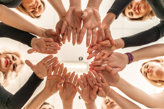 Team of people holding hands. Group of happy young women holding hands. Bottom view, low angle shot of human hands. Friendship and unity concept.