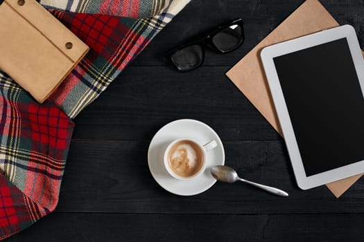 Empty tablet, a cup of coffee, notebook on the desk. Tablet, cup hot coffee on old vintage wooden board. Top view, flat lay. Copy space. Still life. Cafe.