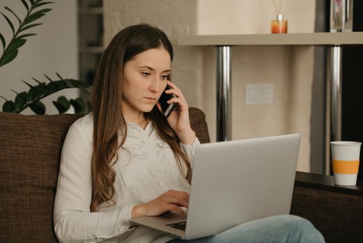 Remote work. A caucasian woman working remotely on her laptop. A businesswoman calls sitting on the couch at home.