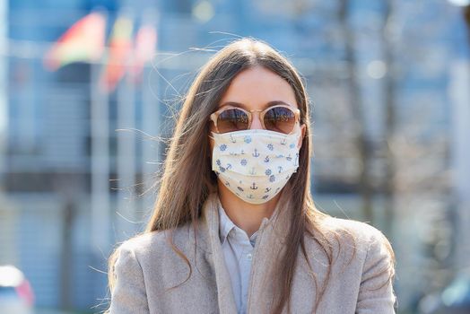 A young woman in a coat wears a medical face mask to avoid the spread of coronavirus. A businesswoman in sunglasses with a surgical mask on the face against COVID-19 in the street.