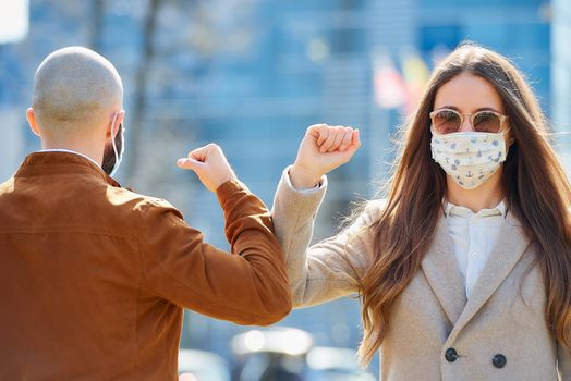 Elbow bumping. Elbow greeting to avoid the spread of coronavirus (COVID-19). Man and woman in the sunglasses meet with bare hands. Instead of greeting with a hug or handshake, they bump elbows.