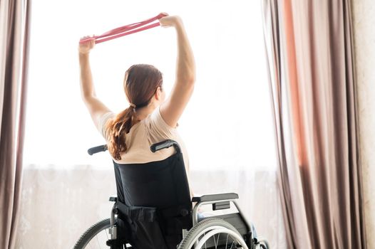 Caucasian woman in a wheelchair doing exercises with the help of fitness rubber bands