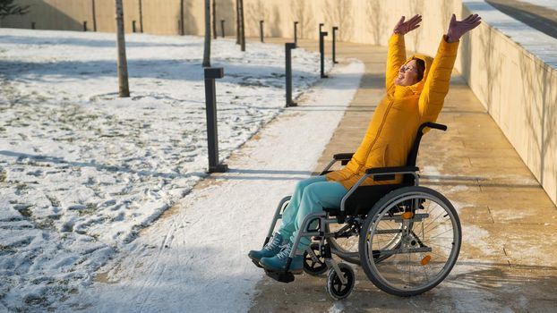 Happy woman in wheelchair happily pulls her hands up while walking in winter park
