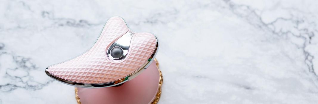 microcurrent facial toning device on pink background with green leaves. Modern beauty skincare concept. top view