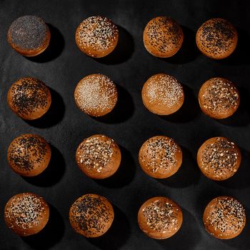 Variety of fresh, tasty baked buns with black and white sesame and sunflower seeds against black background with copy space. Rural cuisine or bakery. Close-up, top view
