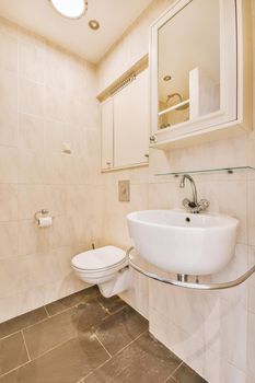 Interior of narrow restroom with sink under the mirror and wall hung toilet with white walls and checkered floor