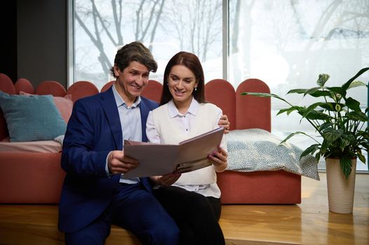 Middle-aged European newlyweds looking through a catalog while visiting an upholstered furniture store. An adorable couple buying a stylish baby sofa bed. Home interior design