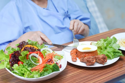 Asian senior or elderly old lady woman patient eating breakfast vegetable healthy food with hope and happy while sitting and hungry on bed in hospital.