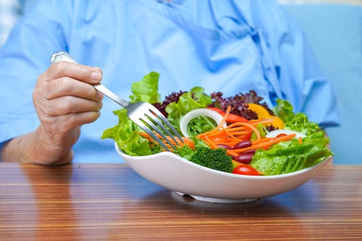 Asian senior or elderly old lady woman patient eating breakfast vegetable healthy food with hope and happy while sitting and hungry on bed in hospital.