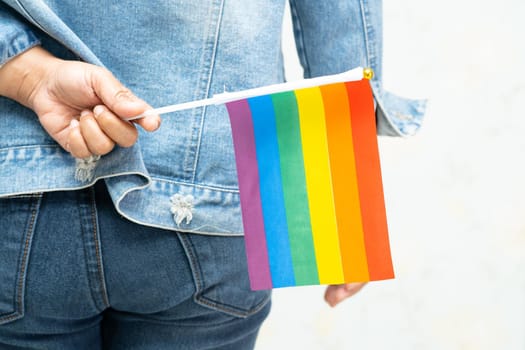 Asian lady wearing blue jean jacket or denim shirt and holding rainbow color flag, symbol of LGBT pride month celebrate annual in June social of gay, lesbian, bisexual, transgender, human rights.