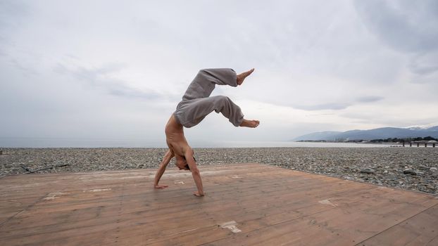 Shirtless caucasian man doing backflip on pebble beach