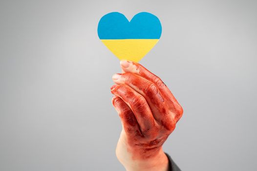Woman with hands covered in blood holding a heart with the flag of ukraine on a white background