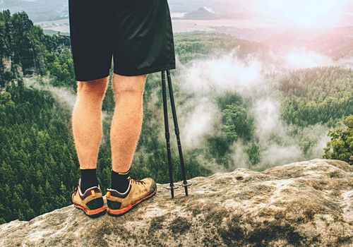 Hiker legs hiking in fall nature. Guy just relax on mountain top and enjoy view.  Feets in trekking shoes and legs short running trousers 