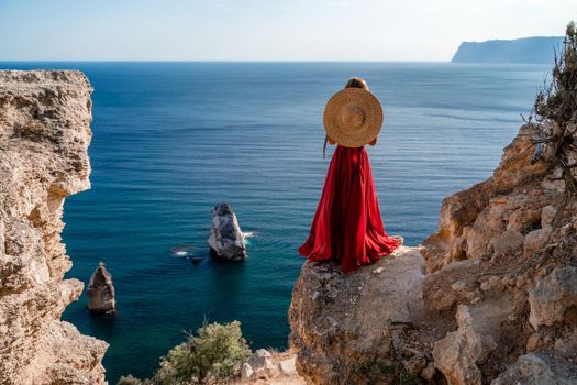 A woman in a flying red dress fluttering in the wind and a straw hat against the backdrop of the sea