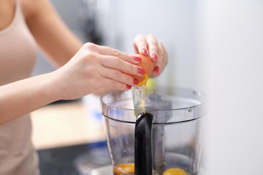 Woman adds eggs to blender for dough. Multicombine for cooking food at home concept