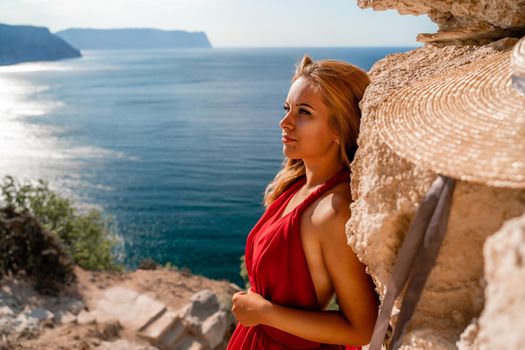 Smiling young woman in a red dress looks at the camera. A beautiful tanned girl enjoys her summer holidays at the sea. Portrait of a stylish carefree woman laughing at the ocean