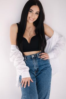 Pretty woman barefoot in studio. Beautiful brunette girl in black topic tiwh white shirt and blue denim jeans. White background of cyclorama.