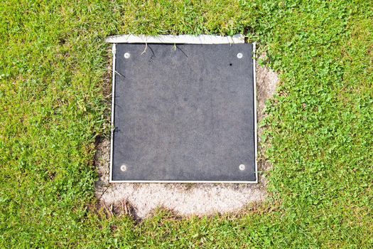 Metal manhole square cover drainage system in the midst of cropped grass
