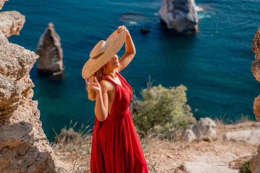 A woman in a flying red dress fluttering in the wind and a straw hat against the backdrop of the sea