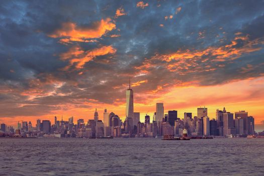 New York City Manhattan downtown skyline at dusk with skyscrapers illuminated over Hudson River panorama. Dramatic sunset sky