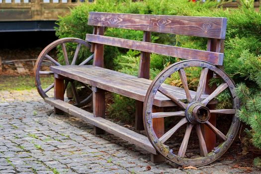 a long seat for several people, typically made of wood or stone.Wooden vintage bench with cart wheels on paving stones.Wooden vintage bench with cart wheels on paving stones. High quality photo