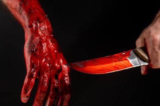 Man holding knife with bloody hand on black background