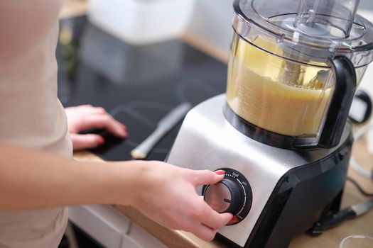 Woman adjusting speed of food processor. Pastry chef in kitchen turns on mixer or food processor concept