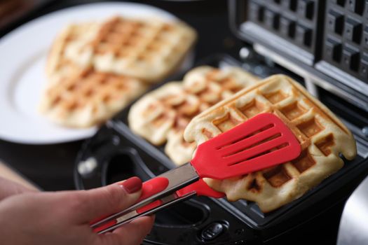 Female hands finishing making waffles on waffle iron in bakery. Persons preparing delicious meals in kitchen