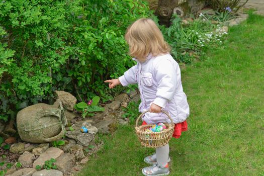 Little girl hunting for easter egg in a spring garden on Easter day