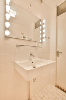 The interior of a bathroom decorated with white tiles with a ceramic sink and a mirror with lighting in a modern house