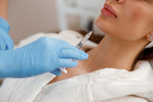 Closeup of young woman getting hyaluronic acid injections in chin at beauty salon. Cosmetology