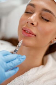 Closeup of young woman getting rejuvenating injections in lips at beauty salon. Cosmetology