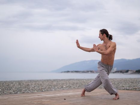 Caucasian man with naked torso practicing wushu on the seashore