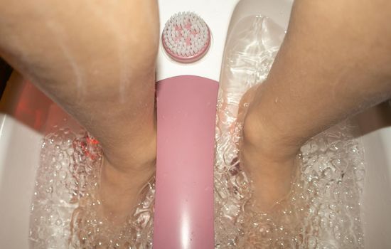 Close-up of feet in a tub with a vibrating foot massager. Electric foot massage bath and water bubbles. Pedicure and foot care.