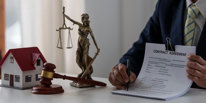 Lawyer in the office with brass scale and pointing in contract on wooden table. Justice and law concept