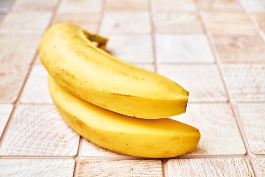 a long curved fruit which grows in clusters and has soft pulpy flesh and yellow skin when ripe.Two ripe bananas on a checkered wooden surface.