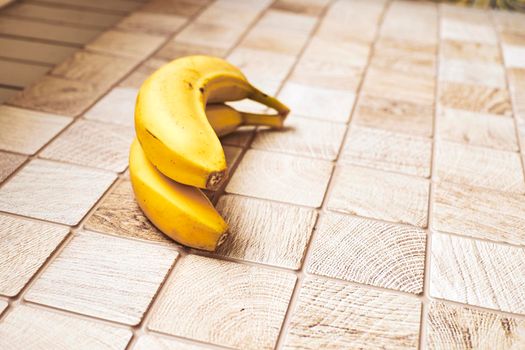 a long curved fruit which grows in clusters and has soft pulpy flesh and yellow skin when ripe.Two ripe bananas on a checkered wooden surface.