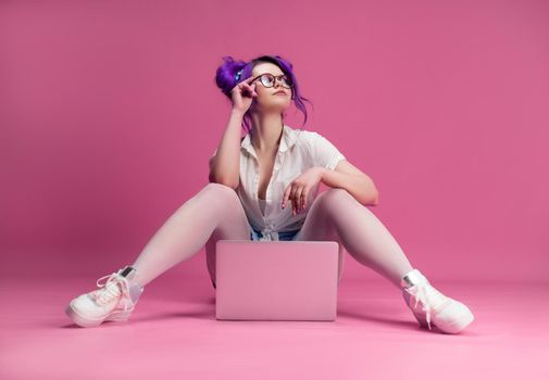 the sexy girl with glasses and purple hair with a laptop on a pink background