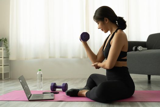 Young asian woman doing fitness exercises at home through virtual class.