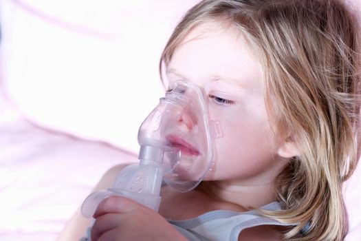 Sick little girl in medical oxygen mask using nebulizer. Long-term home oxygen therapy in children concept