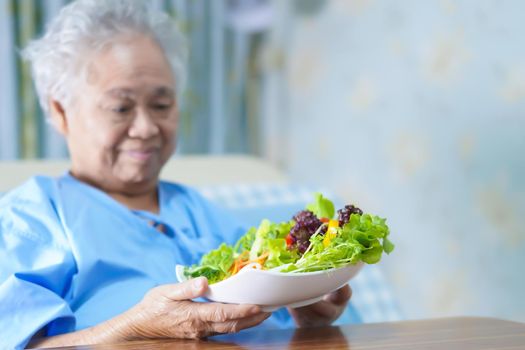 Asian senior or elderly old lady woman patient eating breakfast vegetable healthy food with hope and happy while sitting and hungry on bed in hospital.