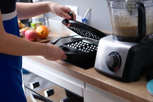 Woman opens electric waffle maker for Viennese and Belgian waffles. Sample kitchen appliance model