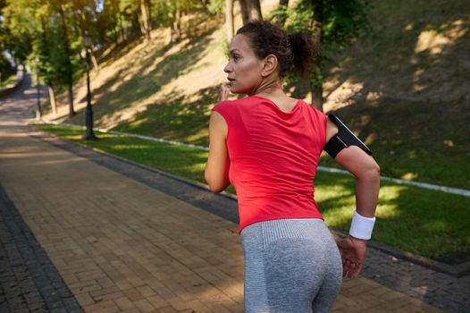 Rear view of an African American woman running on the city park treadmill, enjoying outdoor workout and fitness functional training on a warm sunny summer day. Keep your body fit.