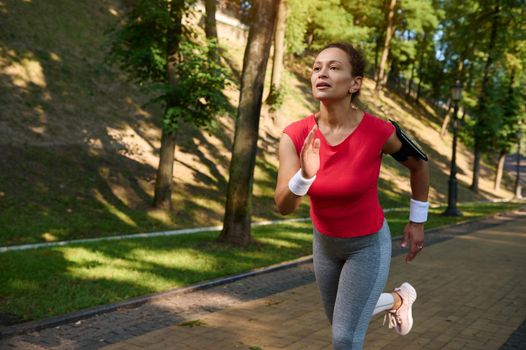 Female runner, charming middle aged sportswoman in tight sportswear enjoying morning jog in the city park on a beautiful summer day