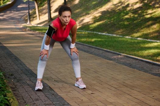 Female runner, Hispanic sportswoman feeling exhaustion while jogging on the running track or treadmill in the city park. Active lifestyle, body weight training, slimming and dieting concept