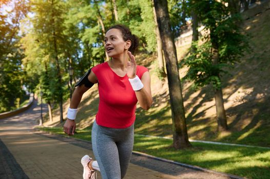 Stunning attractive middle aged fit woman, sportswoman, athlete, runner, jogger running along the treadmill of a city park. Fitness, cardio workout concept