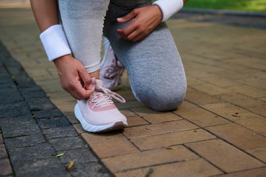 Cropped view of a female athlete, runner tying shoelaces on her sneakers getting ready for jog along the treadmill of a city park. Sport, active lifestyle concept