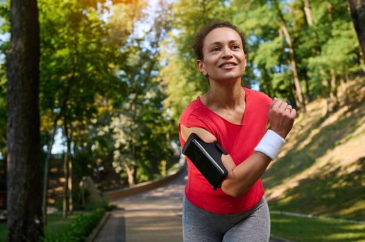 African American young woman, sportswoman, runner runs on a treadmill in a city park, trains on a beautiful sunny summer day. Concept of active lifestyle, sport, fitness, body and health care