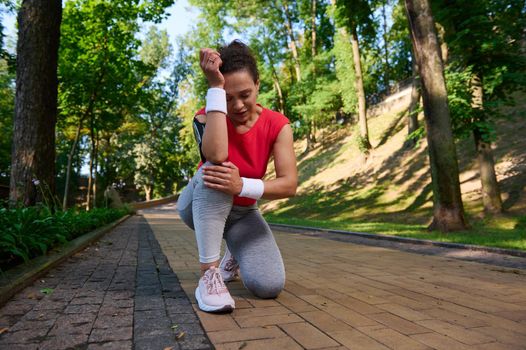 Exhausted sportswoman, female runner feels pain in her knee while running on a path in a forest park. Sports injury, knee pain,sport concept.
