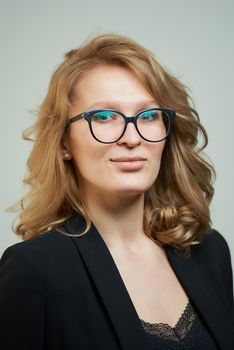 A stylish young woman in glasses dressed in a black suit with a black shirt. A close-up portrait of a blond lady who wears a business outfit. A concept of an office style wardrobe.